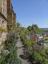 Garden path along a stone wall with a view of a distant castle and houses on a hill under a blue