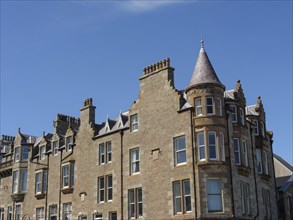 Tall historic building with many chimneys and a prominent tower under a clear blue sky, grey houses
