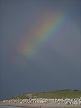 A rainbow appears in the dark sky above a beach, Baltrum Germany