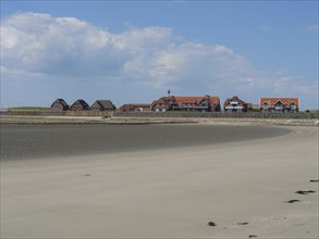 Coastal area with several houses, bordering the beach and the sea, under blue sky with clouds,