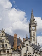 Clock tower and gothic buildings with ornate facades under a blue sky with clouds, skyline of a