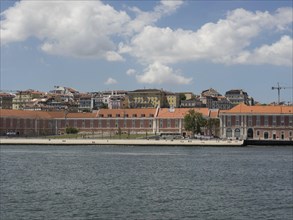 Historic buildings and long wall along the riverside under blue sky and white clouds in Lisbon,