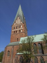 Majestic church tower in brick gothic style with green roofs and trees under a bright blue sky, red