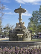 Fountain with several statues and flowing water, surrounded by plants and flowery area, Madrid,