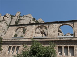 A stone ruin with round arches in front of imposing rocks and a clear blue sky, monastery in rocky