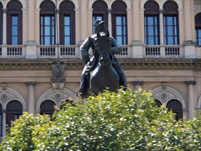 Equestrian statue of a historical figure in front of a classical building surrounded by green