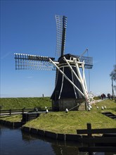 Traditional windmill on a sunny day with people near a canal, Enkhuizen, Nirderlande