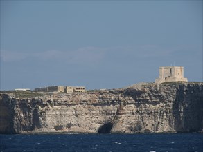Coastal fortress on steep cliffs overlooking the sea, under a clear blue sky, the island of Gozo