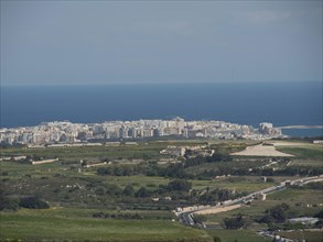 City view on the coast, with green landscape and blue sea in the background, the town of mdina on