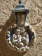 A religious wall decoration with a lamp on a stone wall, the town of mdina on the island of malta