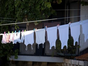 White towels hanging on a washing line, fastened by colourful clips, in the background a balcony