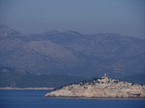 Small island with a building and mountains in the background on the blue sea, the old town of