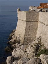 Massive stone walls and rocks directly on the calm blue sea, the old town of Dubrovnik with