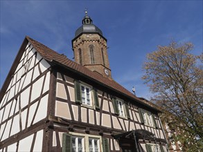Traditional tower and half-timbered house surrounded by trees under a blue sky, historic