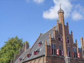 Old brick buildings with spires and red shutters under a blue sky with clouds, red brick houses and