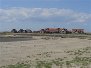 A sandy beach with a row of houses behind it under a blue sky with clouds, Baltrum Germany