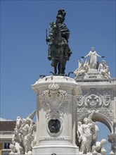 Large equestrian statue on an ornate pedestal in front of an ornate triumphal arch under a clear