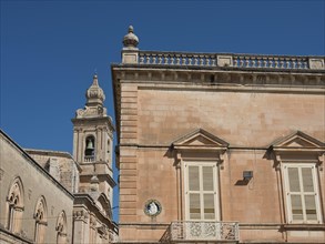 Old buildings with ornate facades and a bell tower against a blue sky, the town of mdina on the