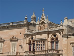 A historic building with ornate windows and stone walls under a blue sky, the town of mdina on the