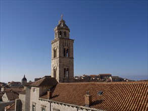 Bell tower above historic tiled roofs against a clear blue sky in an old town, the old town of