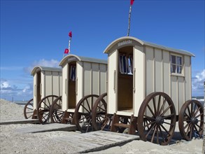 Beach with changing cabins and people on the shore, red flags and blue sky in the background,