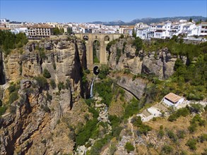 Gorge with old bridge and white houses on the rocks, mountains in the background, sunny day, aerial