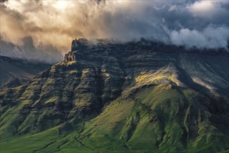 An imposing mountain landscape with dramatic clouds, emphasised by sunlight, creates a fascinating