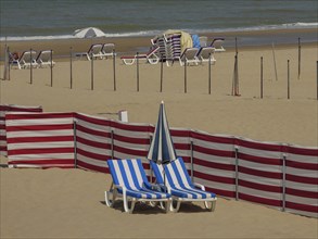 Empty beach with scattered blue and white striped deckchairs, parasols, red partitions and sea