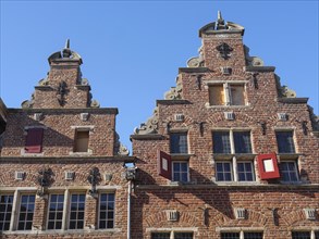 Historic red brick buildings with ornate facades and turrets under a clear blue sky, red brick