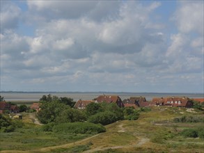 Landscape shot of houses in the dunes with green vegetation and a cloudy sky, Baltrum Germany