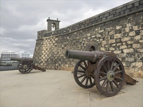 Two old cannons in front of the stone walls of a fortress under a cloudy sky, Lanzarote, Spain,