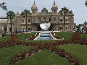 Historic building with palm trees and a decorative fountain in a well-tended garden, Monte Carlo,
