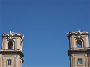 Two symmetrical building towers with sculptures and ornate stonework under a clear blue sky,