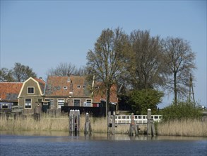 A quiet riverbank with traditional houses and trees in the background, Enkhuizen, Nirderlande