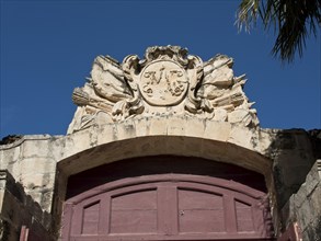 Detailed decorated archway with a coat of arms showing historical motifs under a clear blue sky,