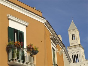 Colourful facade with green shutters, balcony with flowers and a church tower against a clear blue