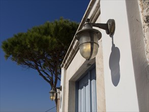 White building with lamp and tree next to it casting a shadow, The volcanic island of Santorini