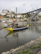 Traditional boat on a river in front of a town with many houses and a hill in the background,