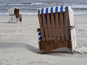 Empty beach chairs on the sandy beach with a view of the calm sea and the slightly cloudy sky,