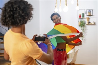 Gay man waving lgbt rainbow flag while couple taking photos with a digital camera at home