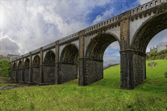 Historic majestic eight-arched bridge over the Ribeira Grande river against a backdrop of grass and