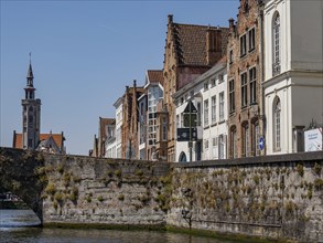Stone bridge and historic facades with a view of a church tower along a canal under a blue sky,