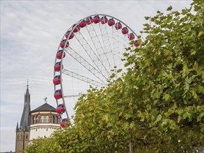 Red Ferris wheel next to a church tower and a historic building behind green trees, Ferris wheel