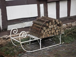 A pile of wood on a white metal sledge in front of an old half-timbered house, kandel, germany