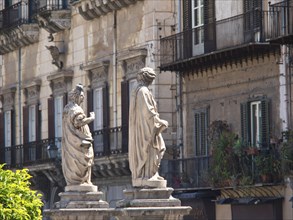 Two statues in front of old buildings with balconies, an antique look with historical architecture,