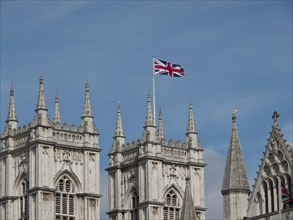 Several gothic towers with a British flag waving against a blue sky, London, England, Great Britain