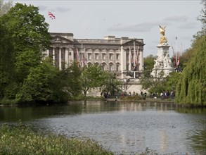 Buckingham Palace and Victoria Monument in the background, in front of it a pond and trees, London,