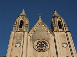 Close-up of a Gothic church with two towers and symmetrical stone facade under a blue sky, Valetta,