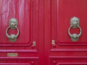 Two shiny red doors with antique, decorative lion's head door knockers, the town of mdina on the
