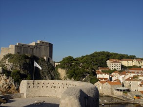 Historic fortress and buildings on a rocky coast with red roofs and sea views under a clear blue